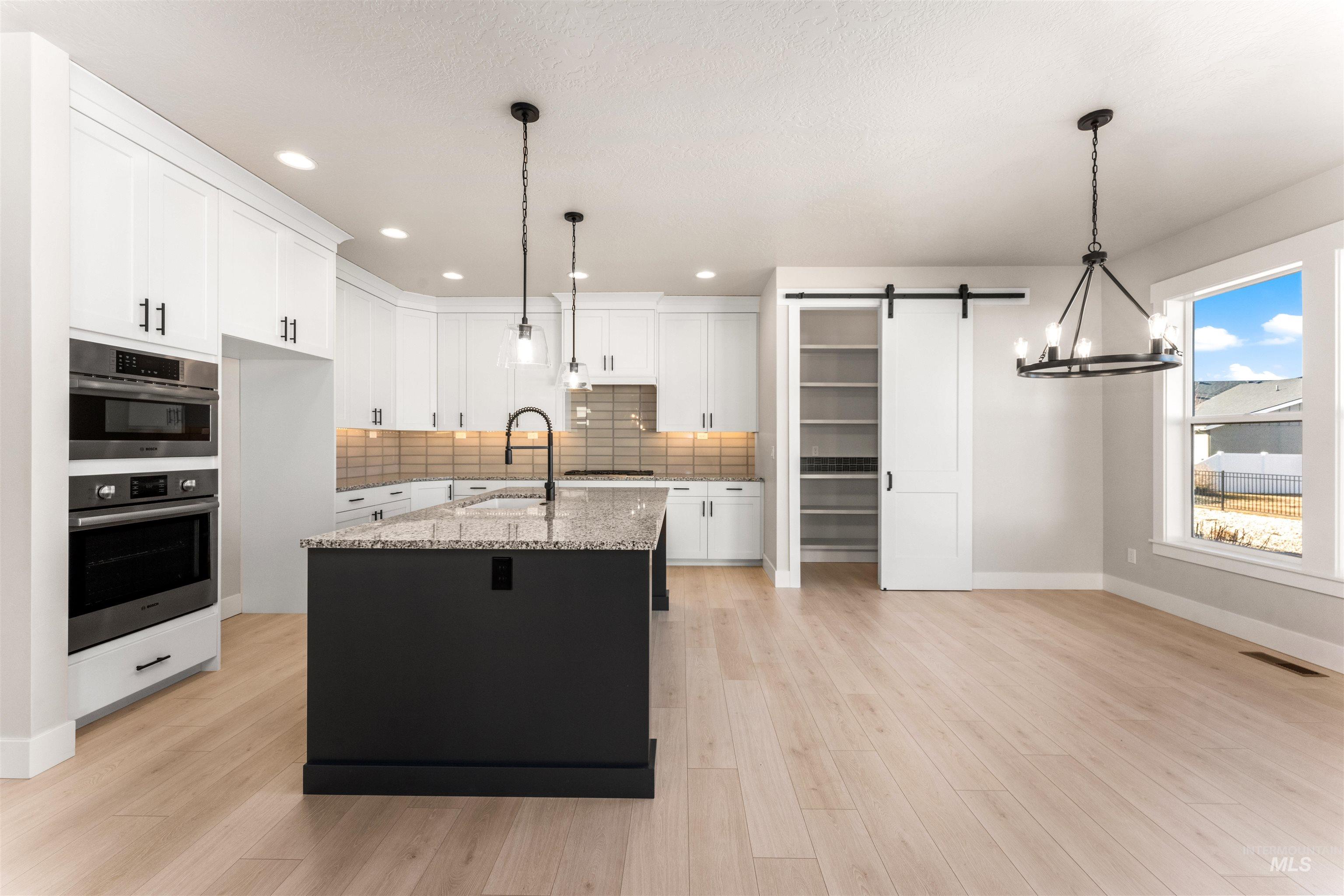 8084 Tandy Cv Street Middleton, ID 83644 - Photo 11 of 46 Kitchen with a barn door, backsplash, light stone countertops, a kitchen island with sink, and light wood-style flooring