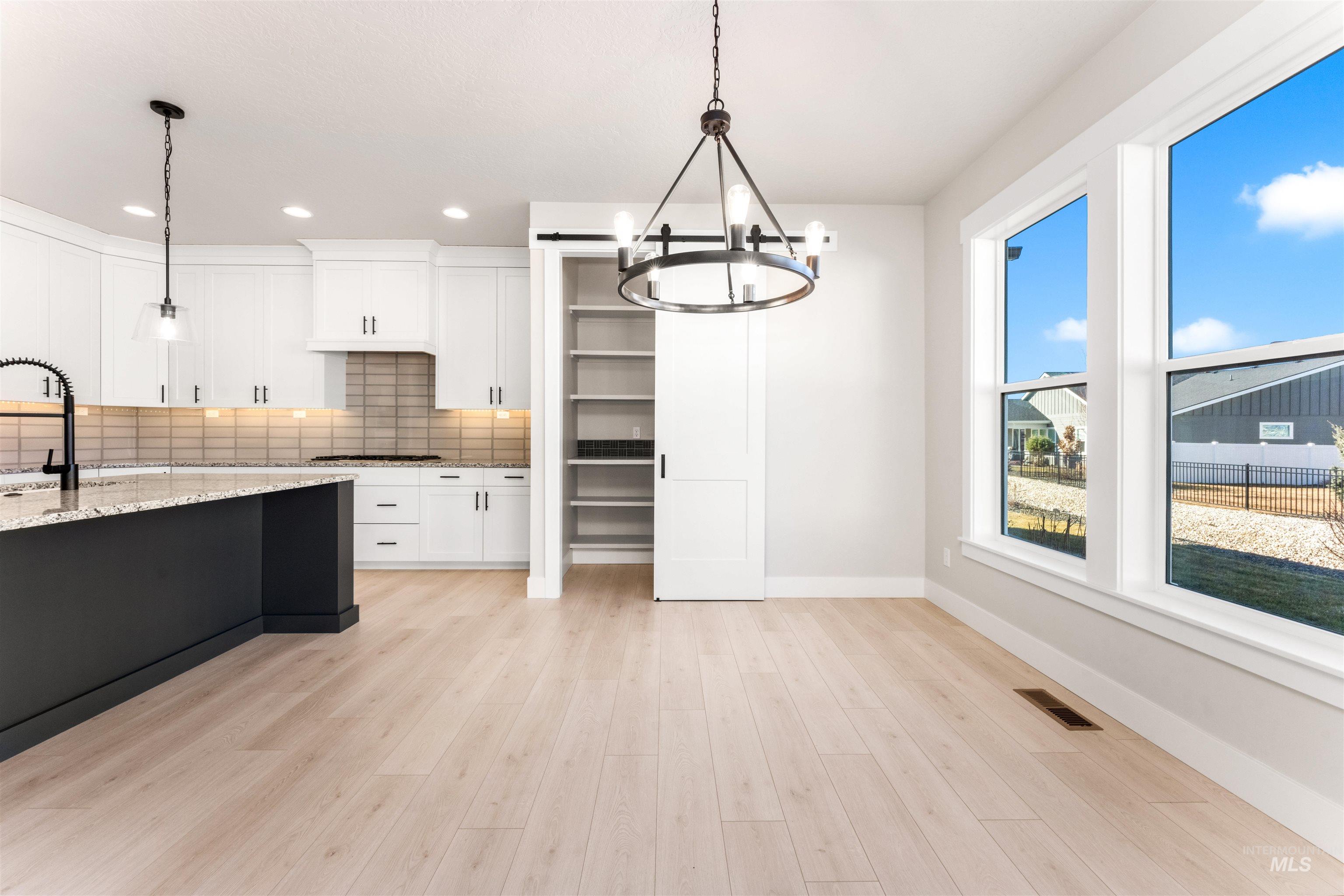 8084 Tandy Cv Street Middleton, ID 83644 - Photo 13 of 46 Kitchen with tasteful backsplash, light stone counters, two tone cabinetry, suspended lighting, and light wood-style floors