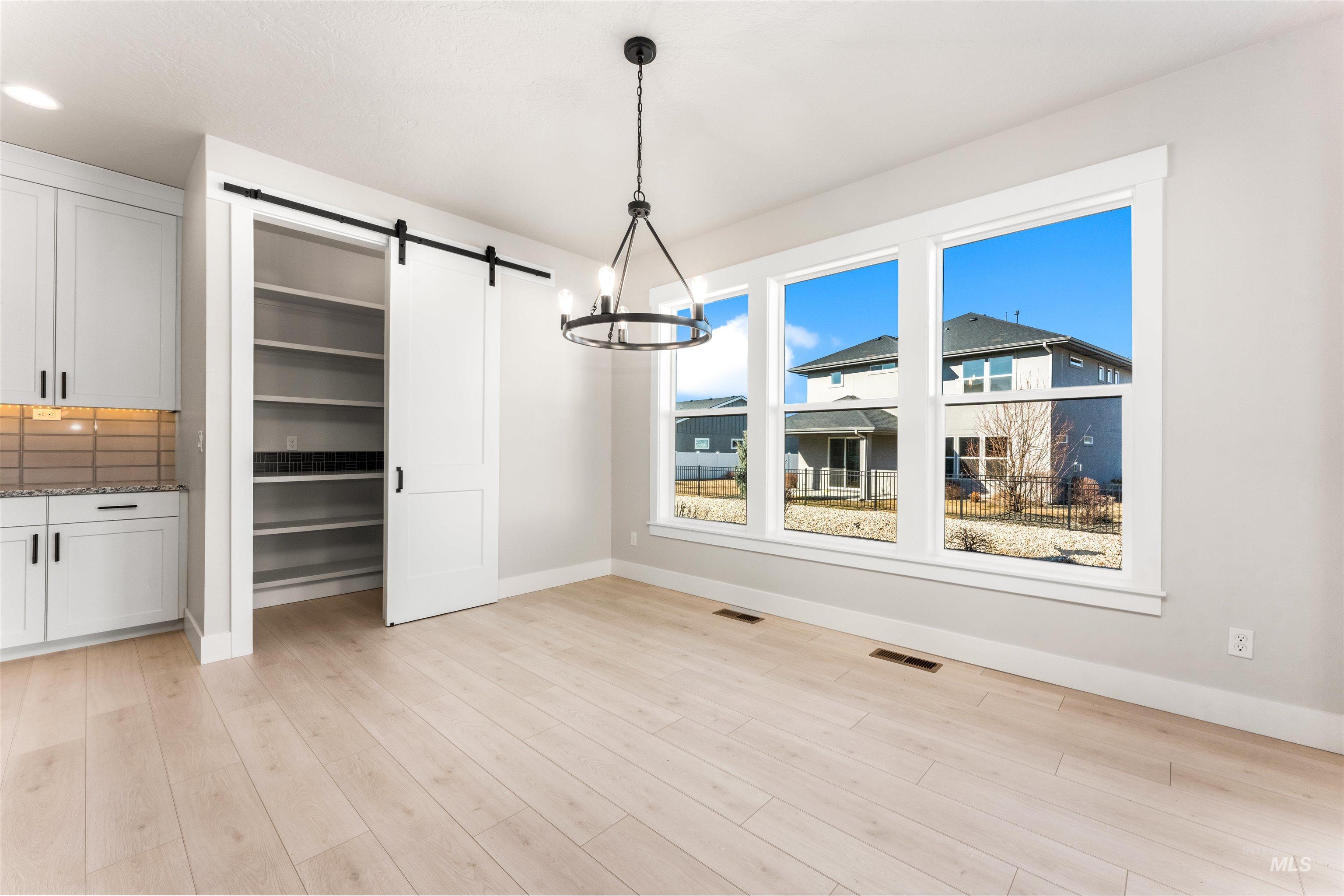 8084 Tandy Cv Street Middleton, ID 83644 - Photo 14 of 46 Unfurnished dining area featuring a barn door, light wood-style floors, and a chandelier