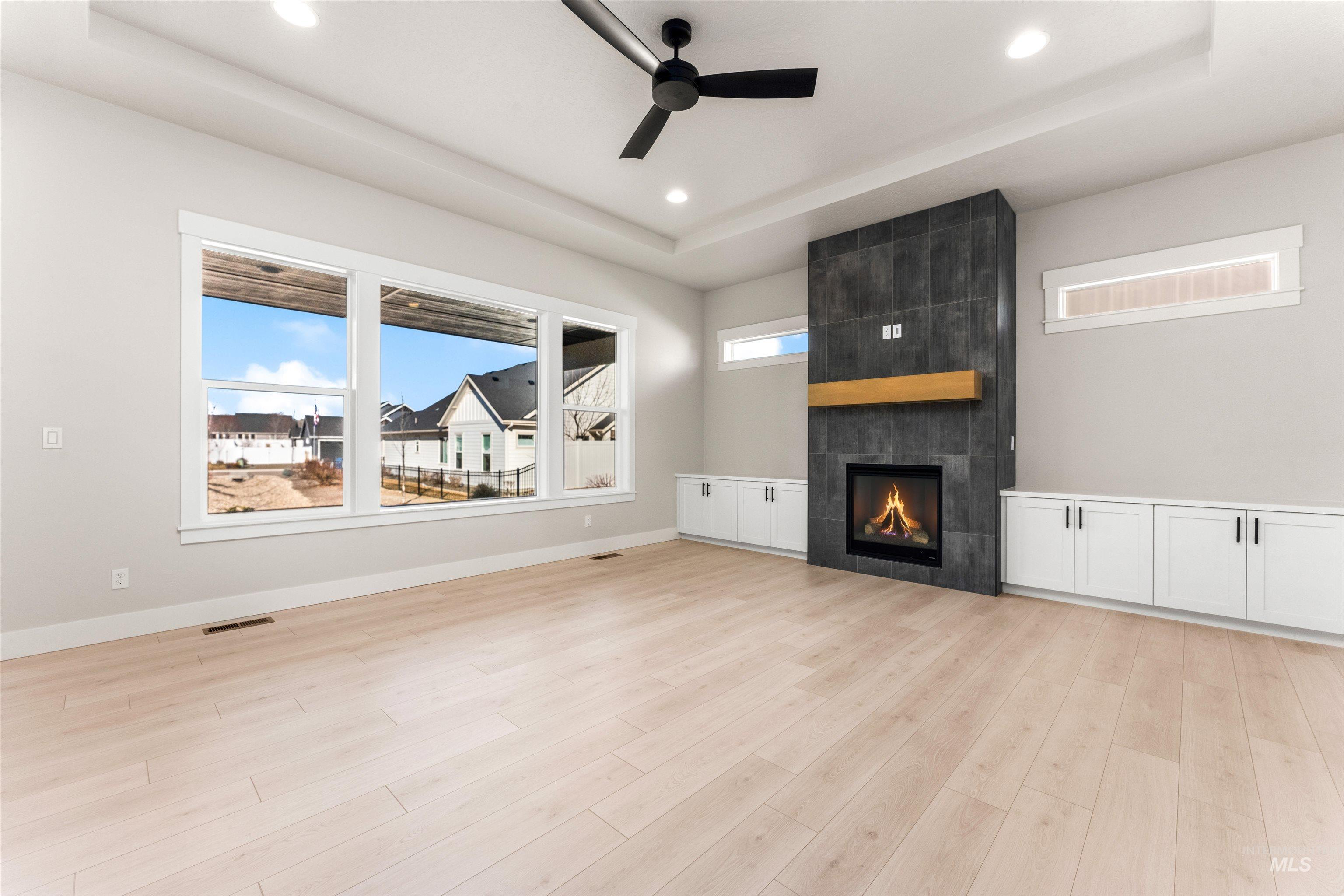 8084 Tandy Cv Street Middleton, ID 83644 - Photo 2 of 46 Unfurnished living room featuring a tray ceiling, a ceiling fan, a tiled fireplace, light wood-type flooring, and recessed lighting