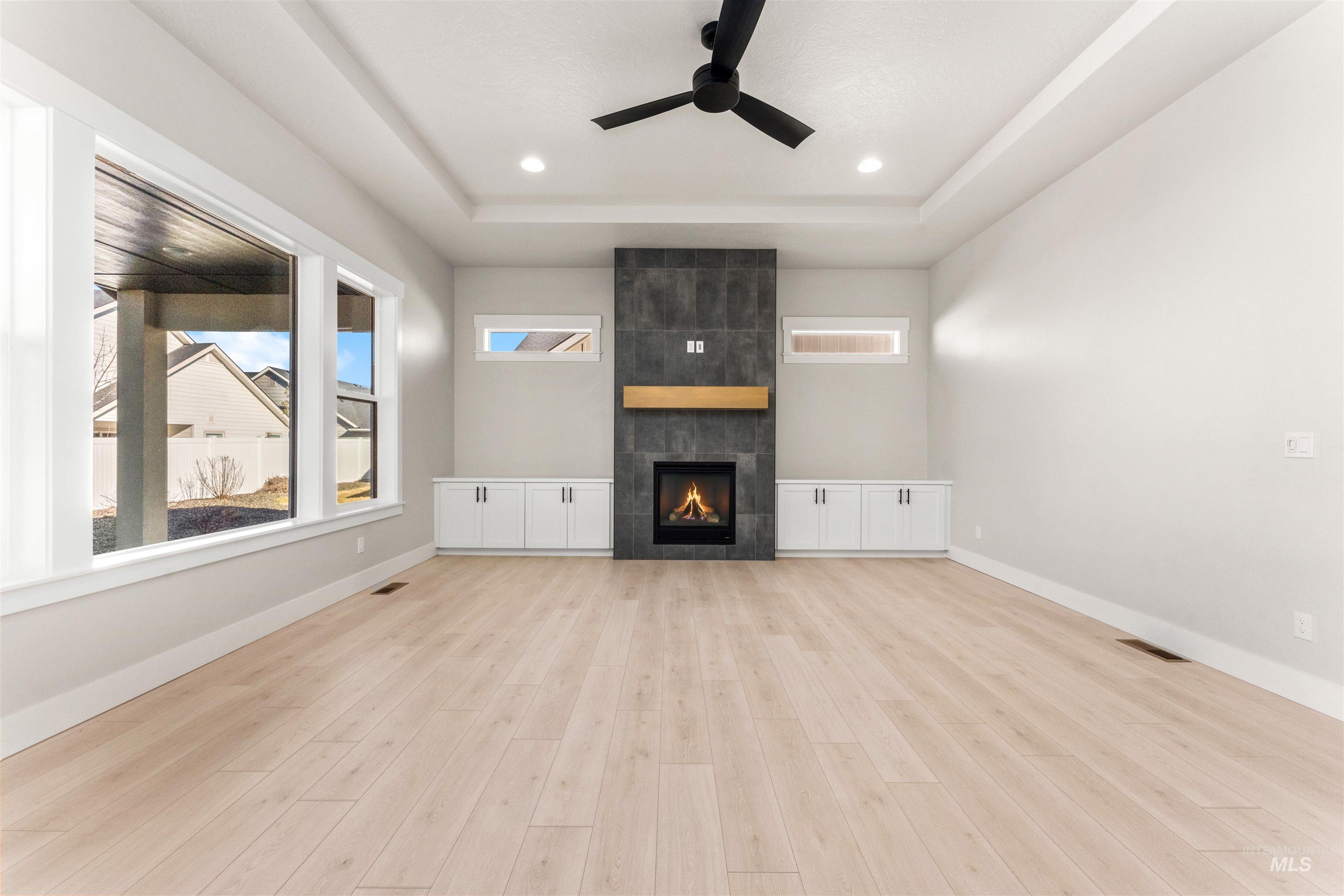 8084 Tandy Cv Street Middleton, ID 83644 - Photo 3 of 46 Unfurnished living room with a raised ceiling, ceiling fan, a fireplace, light wood finished floors, and healthy amount of natural light