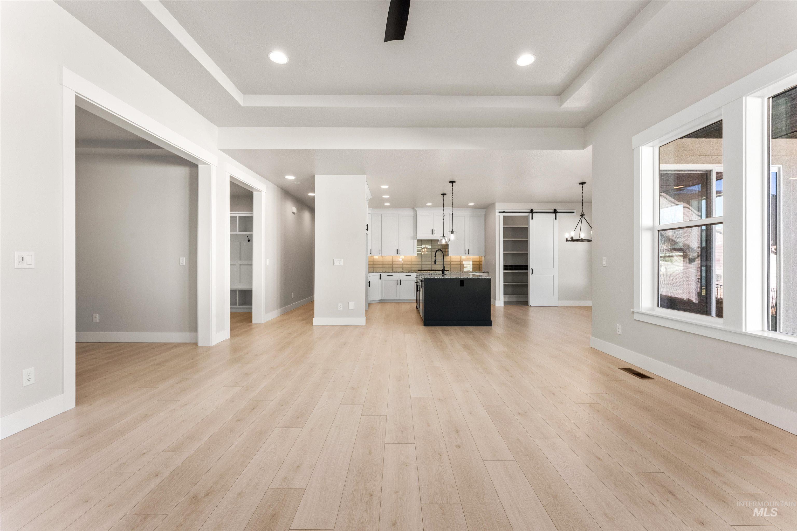 8084 Tandy Cv Street Middleton, ID 83644 - Photo 5 of 46 Unfurnished living room with a barn door, recessed lighting, light wood-style flooring, a raised ceiling, and a ceiling fan