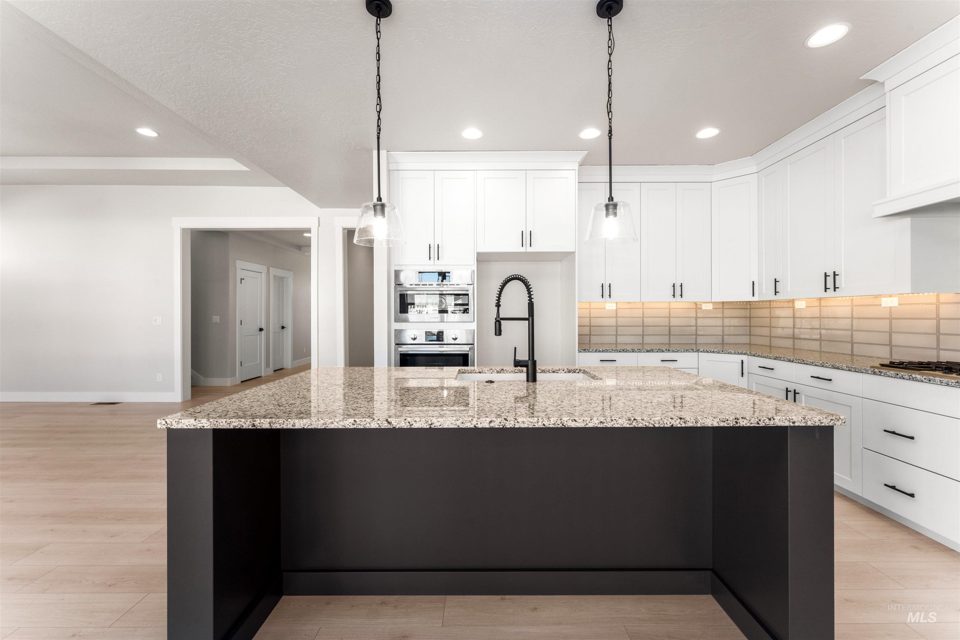 8084 Tandy Cv Street Middleton, ID 83644 - Photo 7 of 46 Kitchen featuring backsplash, light wood-type flooring, light stone counters, a center island with sink, and hanging light fixtures