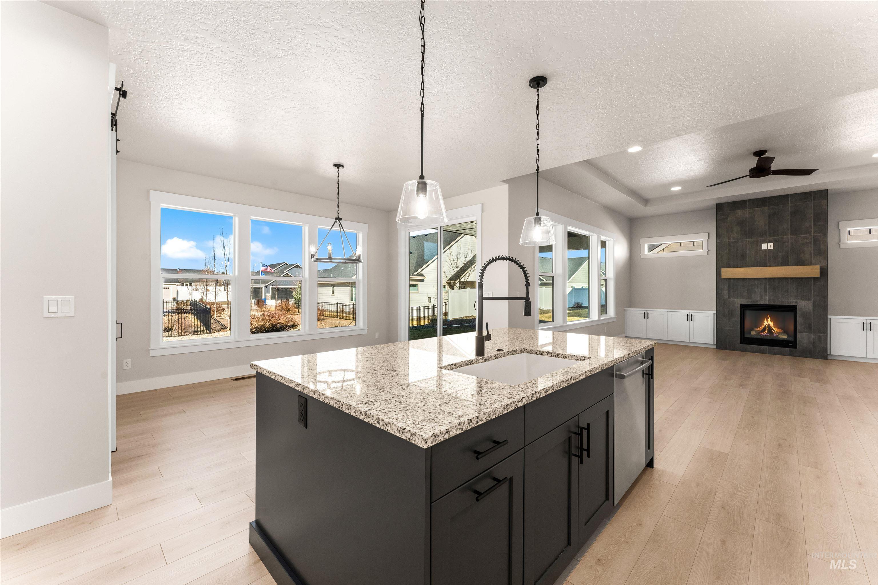 8084 Tandy Cv Street Middleton, ID 83644 - Photo 9 of 46 Kitchen featuring light wood-type flooring, a textured ceiling, a tile fireplace, ceiling fan, and plenty of natural light