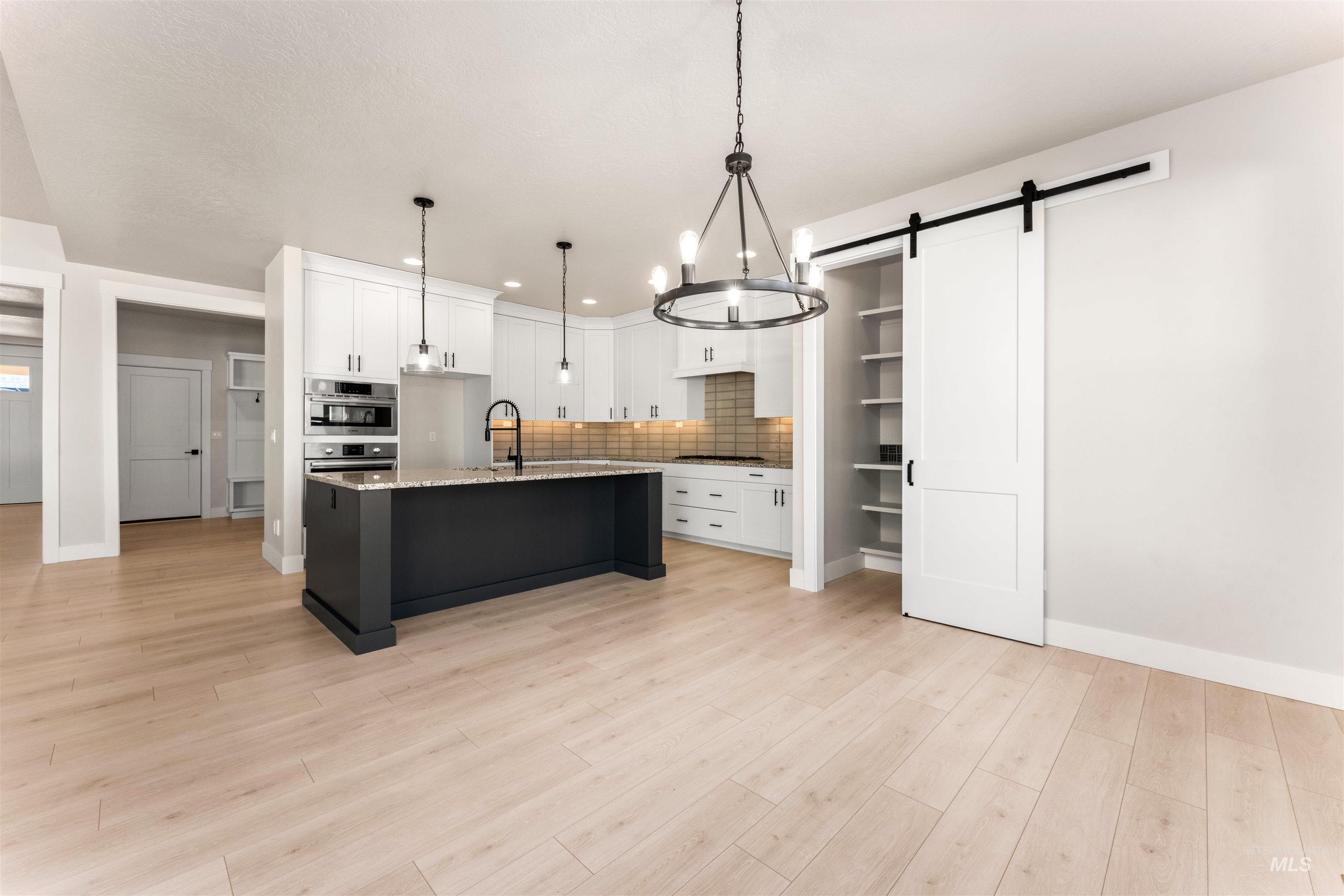 8084 Tandy Cv Street Middleton, ID 83644 - Photo 10 of 46 Kitchen featuring a barn door, a center island with sink, decorative backsplash, light stone countertops, and light wood finished floors