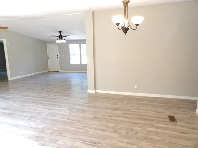 an empty room with wooden floor ceiling fan and window