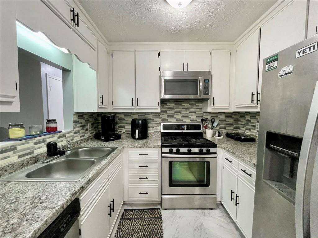 766 Country Club Road Newnan, GA 30263 - Photo 13 of 34 Kitchen featuring appliances with stainless steel finishes, tasteful backsplash, white cabinets, and a textured ceiling