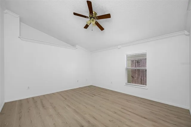 an empty room with wooden floor ceiling fan and windows
