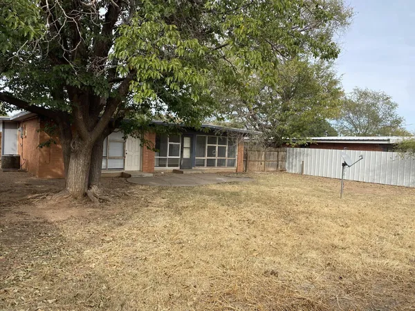 a backyard of a house with large trees and brick wall