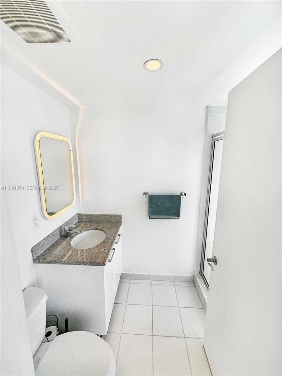 185 Southwest 7th Street, Unit 2701 Miami, FL 33130 - Photo 20 of 24 a bathroom with a granite countertop sink a toilet a mirror and shower