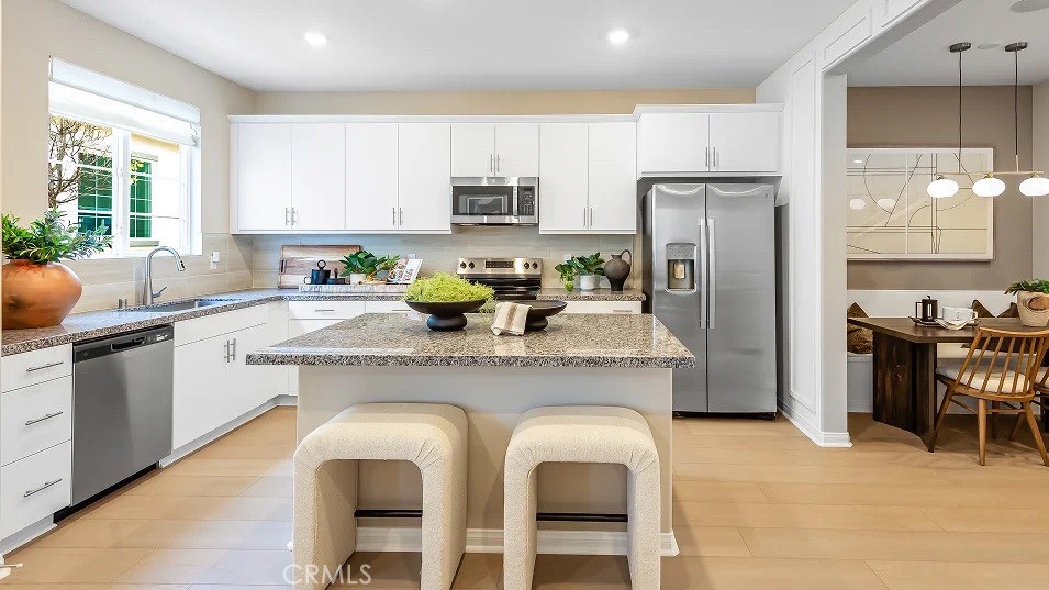 a kitchen with stainless steel appliances granite countertop a sink a stove a refrigerator cabinets and chairs