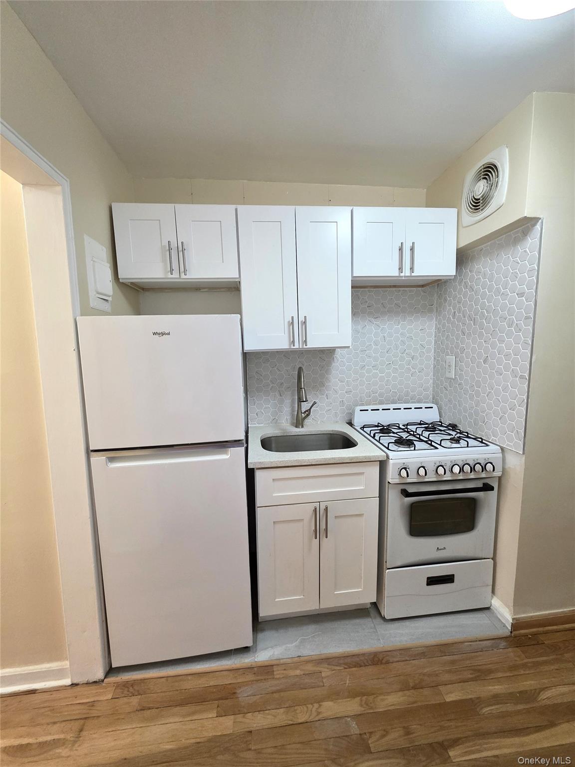 65-05 Yellowstone Boulevard, Unit 6C Queens, NY 11375 - Photo 6 of 11 Kitchen featuring white appliances, white cabinets, tasteful backsplash, light wood-style floors, and light stone counters
