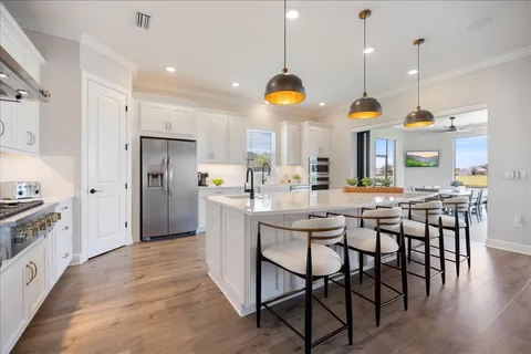 a kitchen with stainless steel appliances granite countertop a stove a refrigerator a oven a sink a dining table and chairs with wooden floor