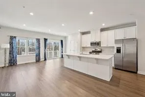 a kitchen with stainless steel appliances granite countertop a refrigerator a sink a stove and white cabinets with wooden floor