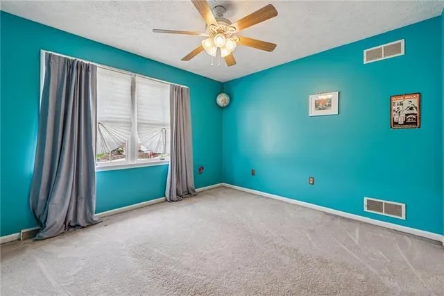 an empty room with window ceiling fan and a kitchen view