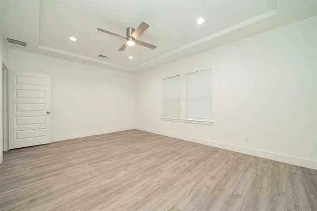 an empty room with wooden floor ceiling fan and windows