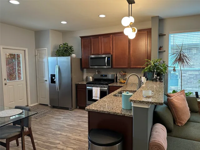 a kitchen with granite countertop stainless steel appliances a stove refrigerator a microwave a stove and a dining table with wooden floor