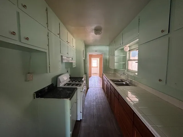 a kitchen with stainless steel appliances granite countertop a stove a sink a refrigerator white cabinets and wooden floor