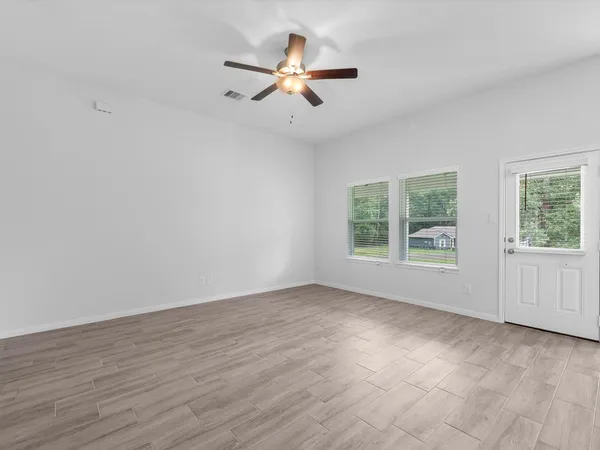 an empty room with wooden floor fan and windows