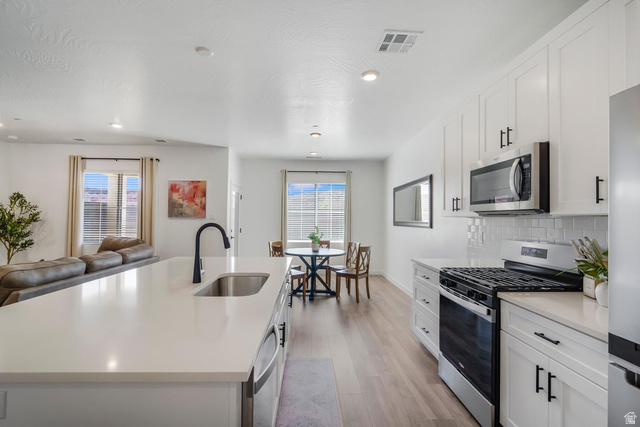 1705 Ripple Rock Drive, Unit 3017 Washington, UT 84780 - Photo 3 of 22 Modern kitchen featuring white shaker cabinetry, stainless steel appliances, a large island with an undermount sink, a subway tile backsplash, and light wood-finish flooring