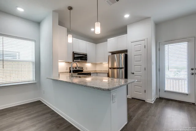 a kitchen with stainless steel appliances granite countertop a refrigerator a sink dishwasher a stove and white countertops with wooden floor