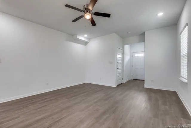 an empty room with wooden floor a ceiling fan and windows