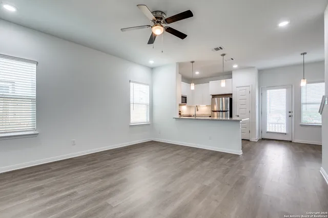 a view of an empty room and kitchen with wooden floor