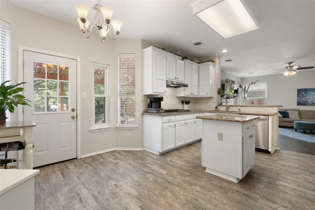 a kitchen with kitchen island granite countertop a stove a sink a refrigerator and white cabinets with wooden floor