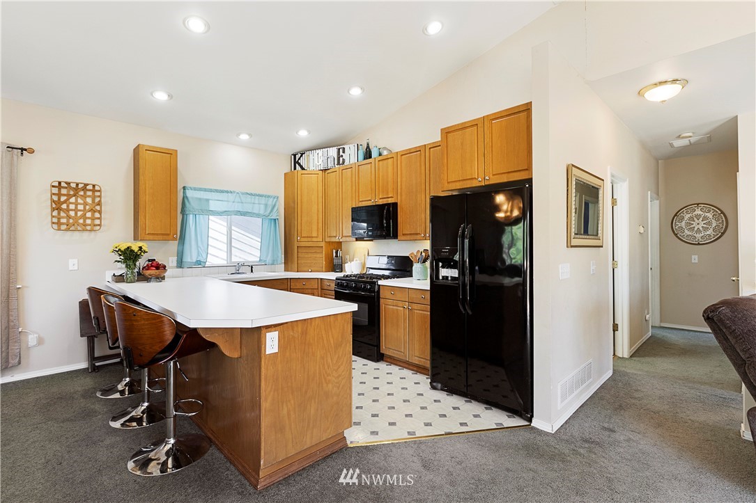 26410 218th Avenue Southeast Maple Valley, WA 98038 - Photo 8 of 28 a kitchen with stainless steel appliances kitchen island granite countertop a refrigerator a stove a sink a dining table and chairs with wooden floor