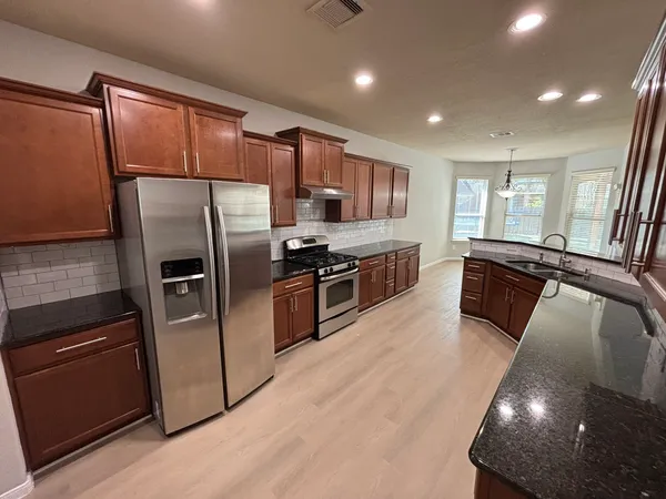 a kitchen with stainless steel appliances granite countertop a refrigerator a sink a stove and a microwave