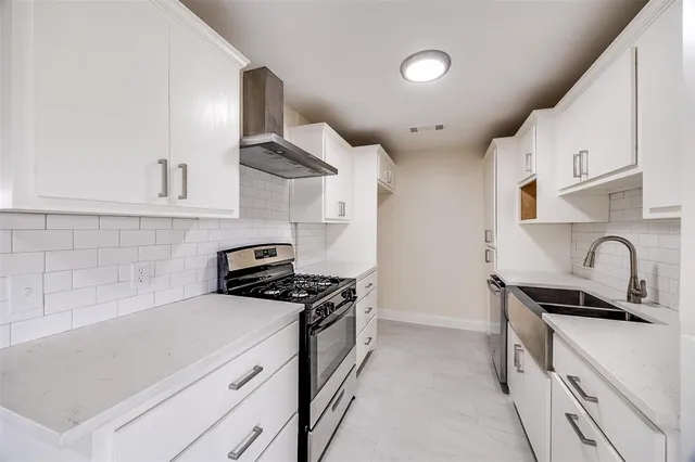 a kitchen with stainless steel appliances a sink dishwasher stove and white cabinets with wooden floor