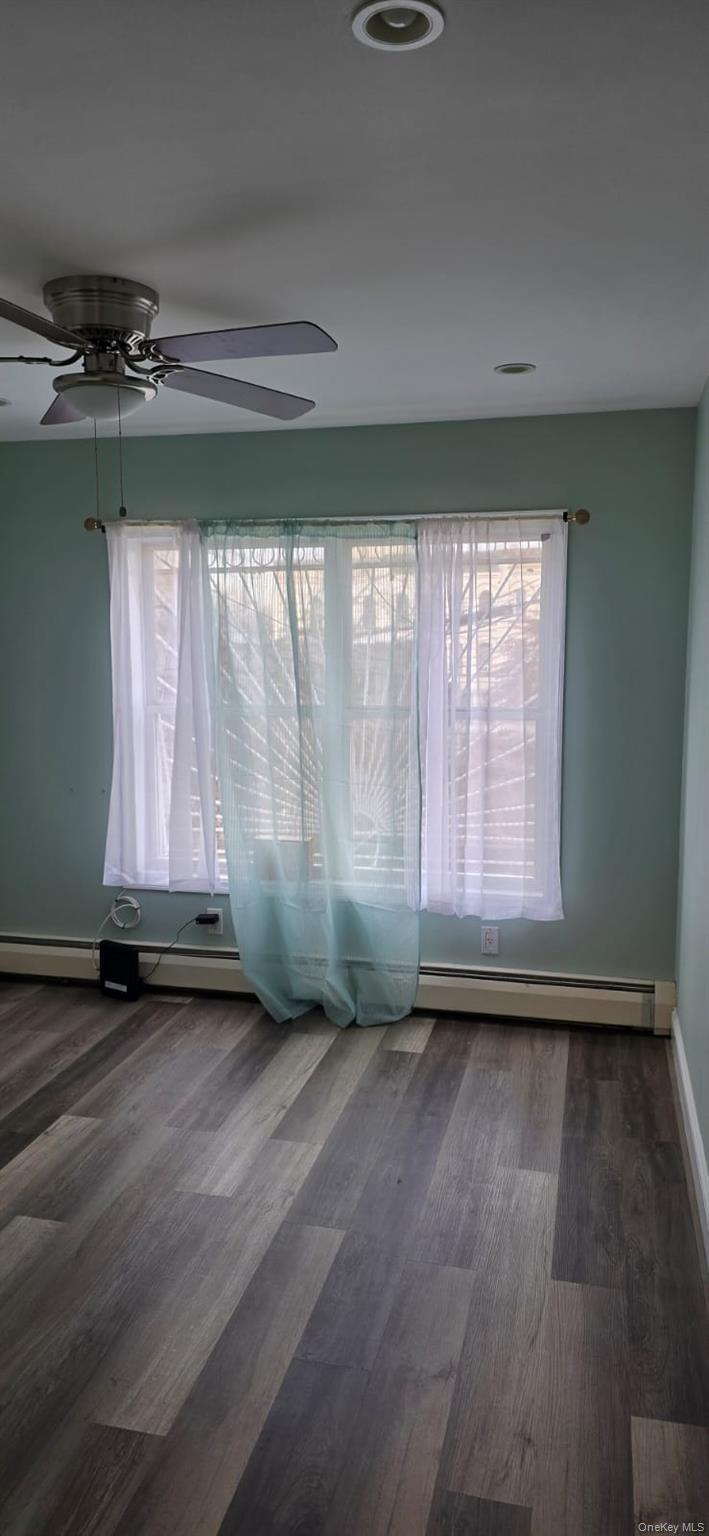 235 MacDougal Street Brooklyn, NY 11233 - Photo 4 of 21 Empty room featuring ceiling fan, dark wood-style floors, and a baseboard radiator