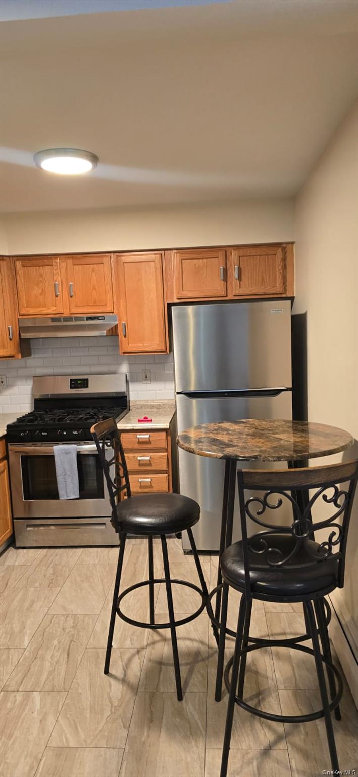 235 MacDougal Street Brooklyn, NY 11233 - Photo 8 of 21 Kitchen with stainless steel appliances, brown cabinetry, backsplash, light countertops, and under cabinet range hood