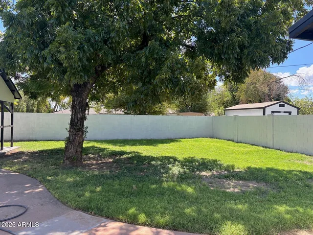 a white house with a big yard plants and large trees