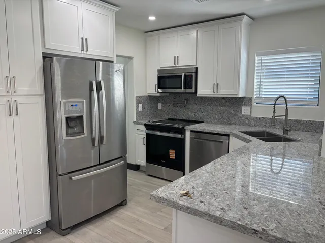 a kitchen with stainless steel appliances granite countertop a refrigerator a sink a stove and oven