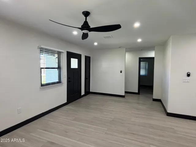 a view of an empty room with wooden floor and a ceiling fan