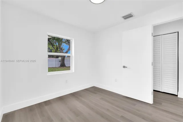 a view of an empty room with wooden floor and a window