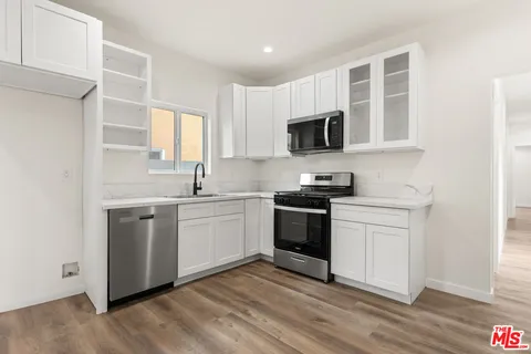 a kitchen with stainless steel appliances granite countertop white cabinets a sink a stove a microwave and wooden floors
