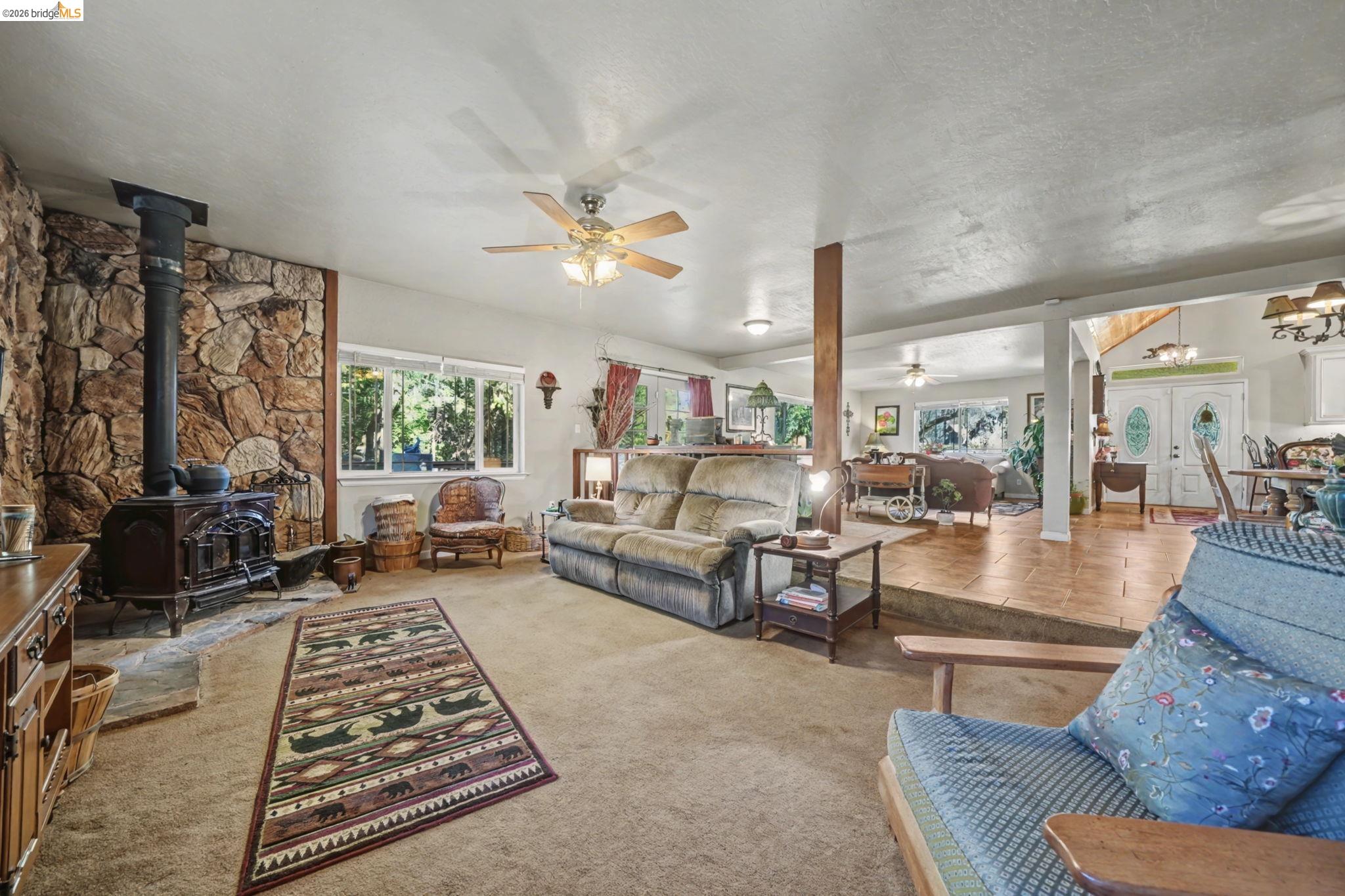 6145 Swiss Ranch Road Mountain Ranch, CA 95246 - Photo 27 of 60 Living room with a wood stove, a chandelier, carpet flooring, ceiling fan, and a textured ceiling