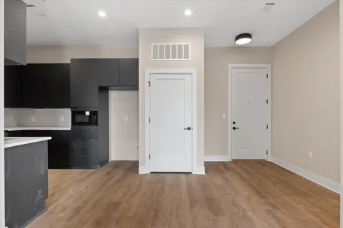 a view of an empty room with kitchen and wooden floor