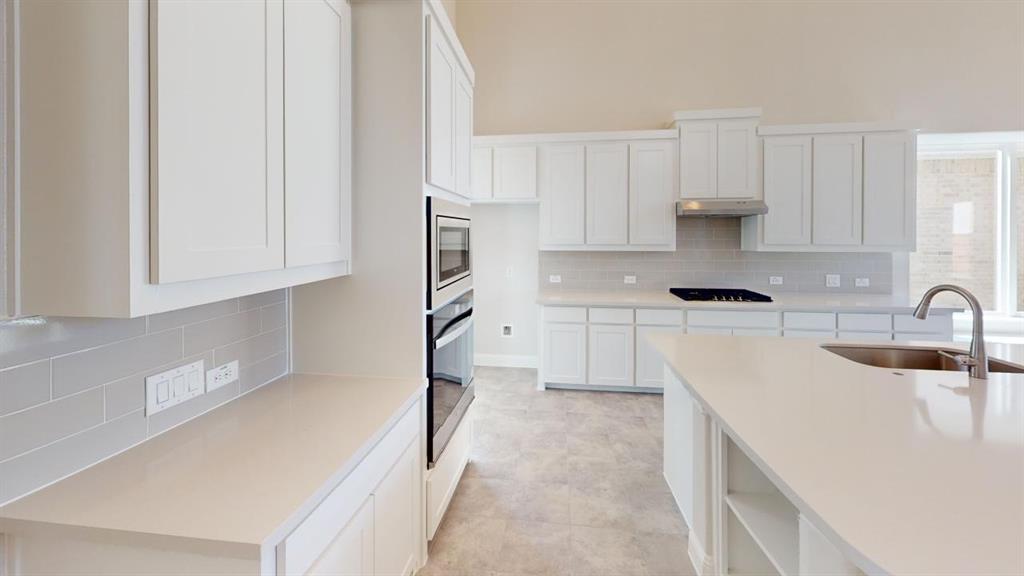 8407 Cornerstone Drive Rowlett, TX 75088 - Photo 23 of 25 Kitchen featuring a center island with undermount sink, white shaker cabinetry, light-toned countertops, a subway tile backsplash, and built-in stainless steel appliances