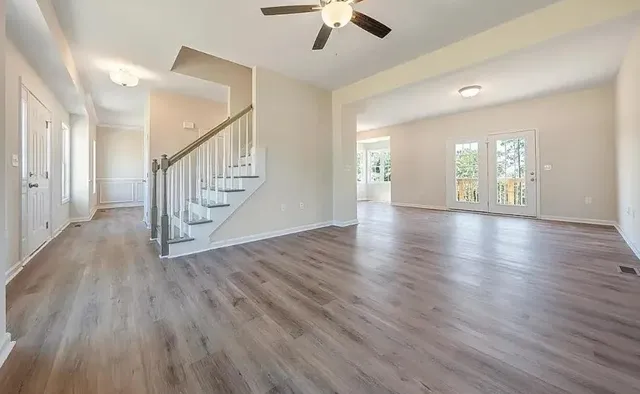 a view of an empty room with wooden floor and a chandelier fan