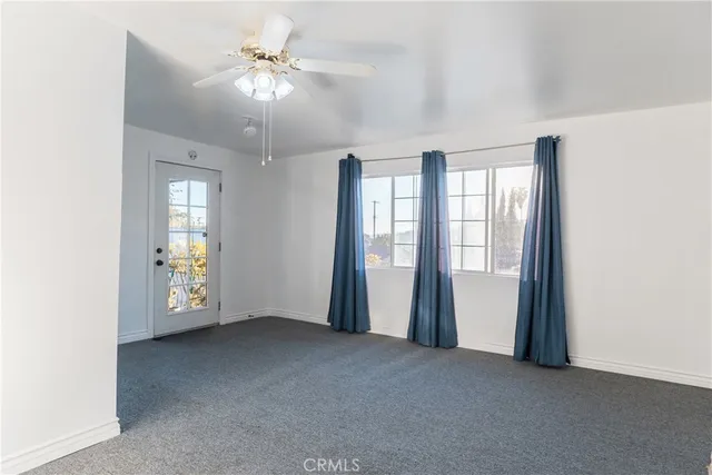an empty room with chandelier fan and windows
