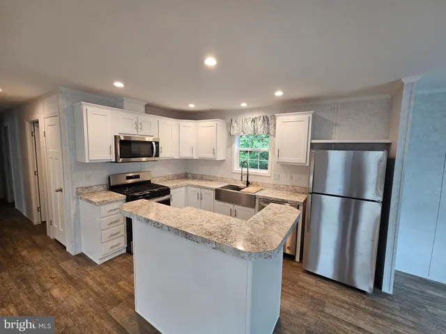 a kitchen with granite countertop a refrigerator a sink a stove a microwave a center island and wooden floor