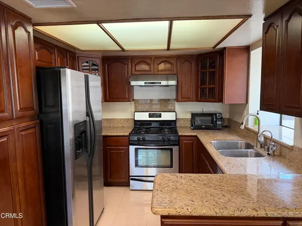 a kitchen with stainless steel appliances granite countertop a refrigerator a stove and a sink with wooden cabinets