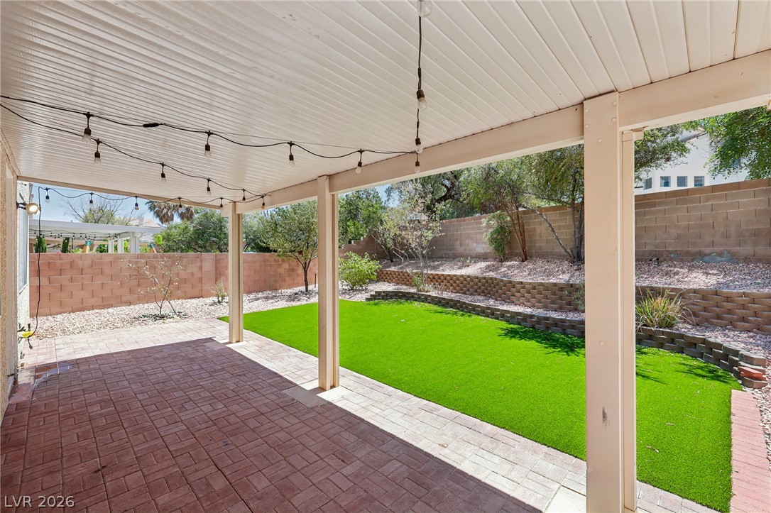 1727 Millstream Way Henderson, NV 89074 - Photo 43 of 46 An inviting covered patio with brick pavers extends to a vibrant green lawn.