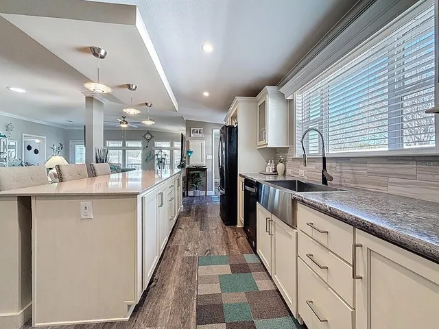 a large white kitchen with a large counter top a sink a window and stainless steel appliances