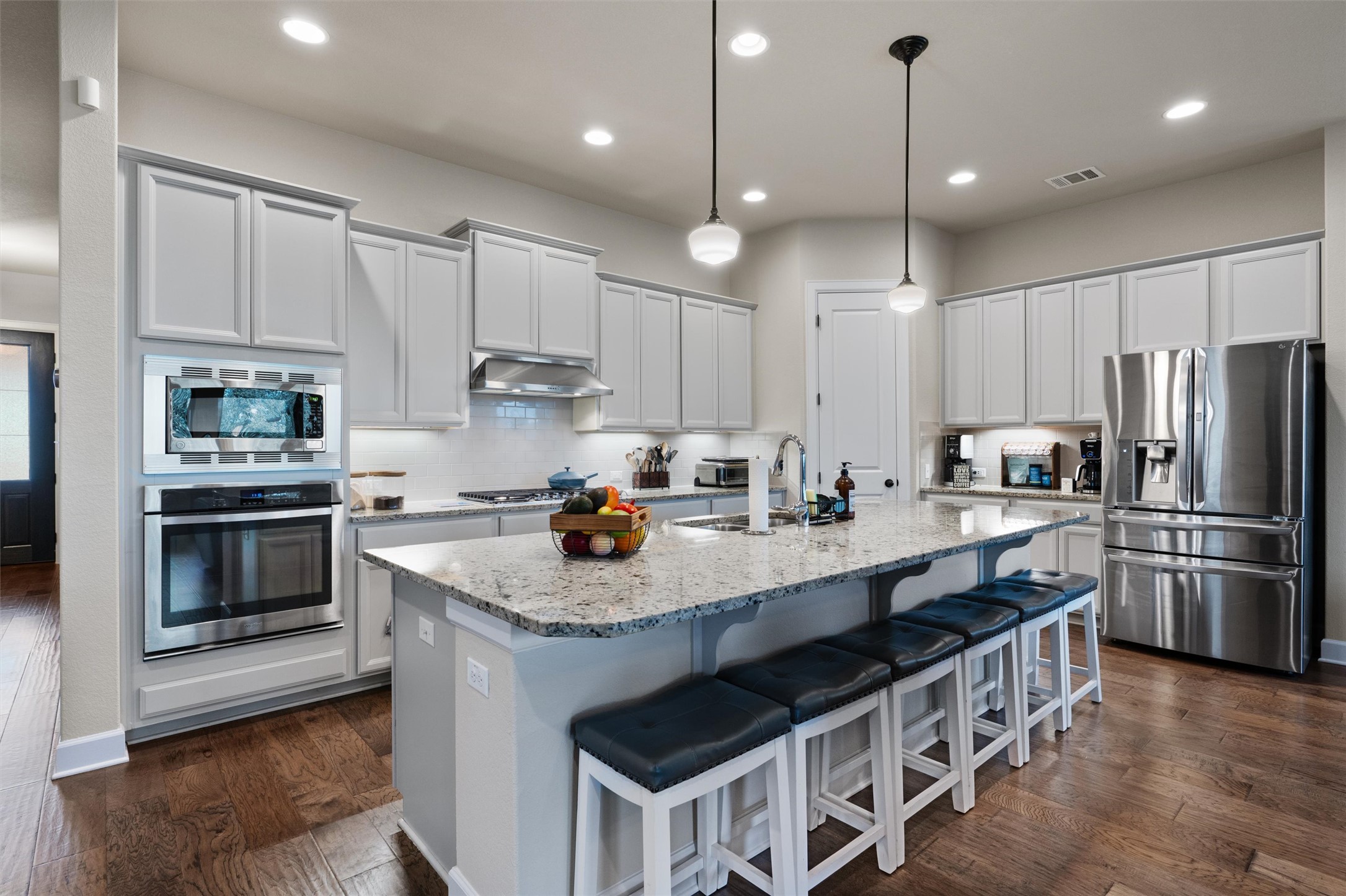 Kitchen with light gray cabinets, stainless steel appliances, a large island with breakfast bar, granite countertops, and dark wood-look tile floors