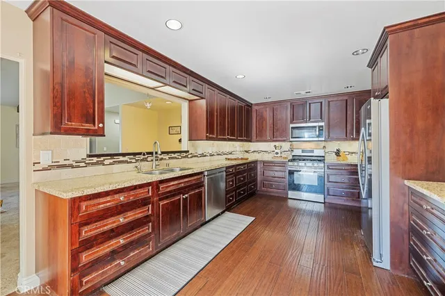a kitchen with granite countertop wooden floors stainless steel appliances and a window