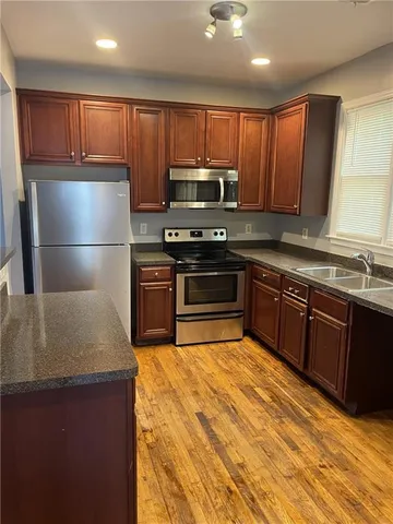 a kitchen with kitchen island granite countertop wooden cabinets a stove a sink and a refrigerator with wooden floor